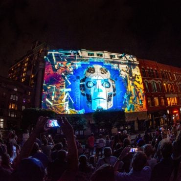 A crowd watches colorful projection mapping illuminate a downtown Binghamton building at LUMA
