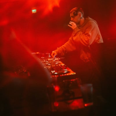 DJ performing over turntables in red light and smoke