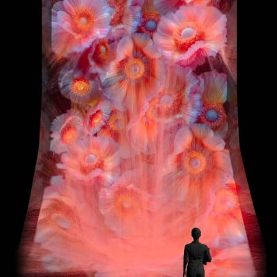 A person standing before Tatsuru Arai's glowing floral waterfall projection in Lux Vitae