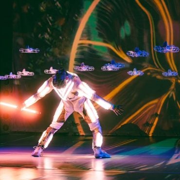 Singularity performer surrounded by synchronized illuminated drones