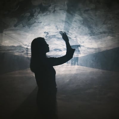 Silhouetted figure moving through projected light and haze in THRESHOLD